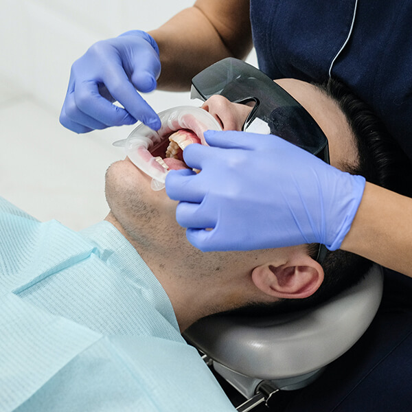 A male patient lying in a dental chair wearing dental glasses and a dental bib during a procedure