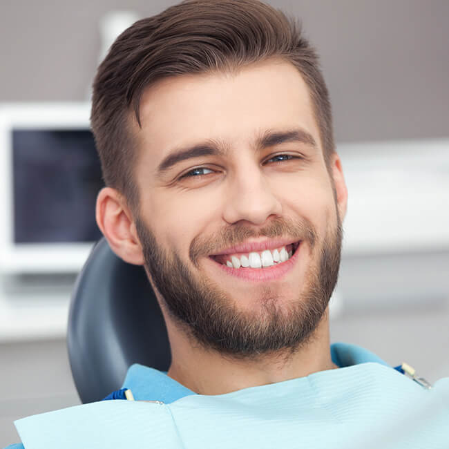 A man with a beard sitting in a dental chair  wearing a dental bib with brilliant smile 
