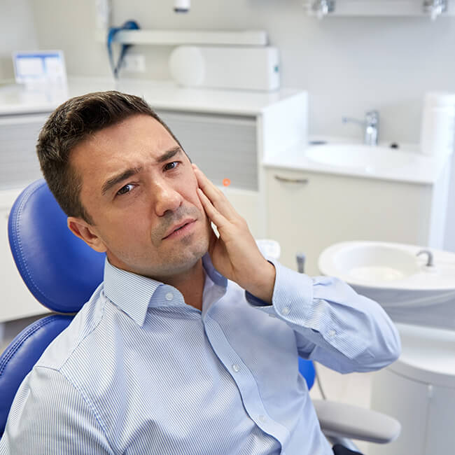 A male patient sitting in a dental chair holding his cheek