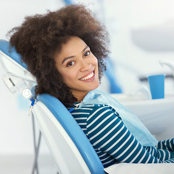A female patient wearing a stripes long sleeve sitting in a dental chair with bright smile