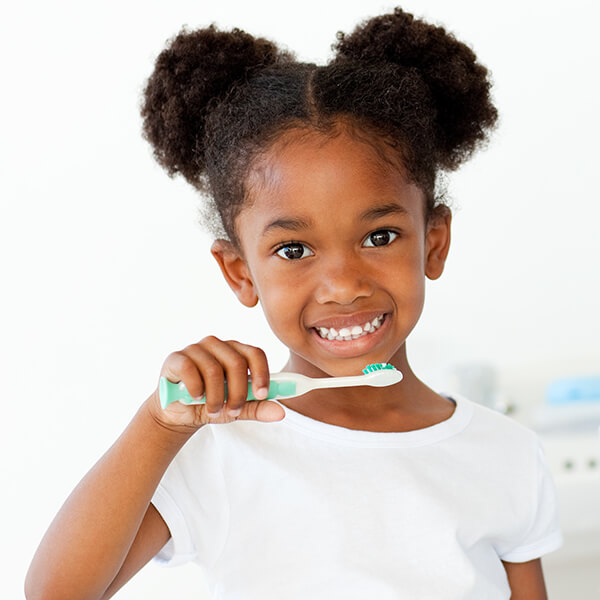 A little girl wearing a white shirt smiling while holding a green toothbrush 