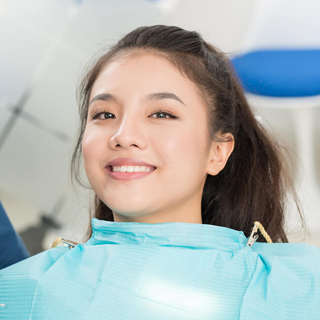 A young female  sitting in a dental chair smiling and wearing a dental gown
